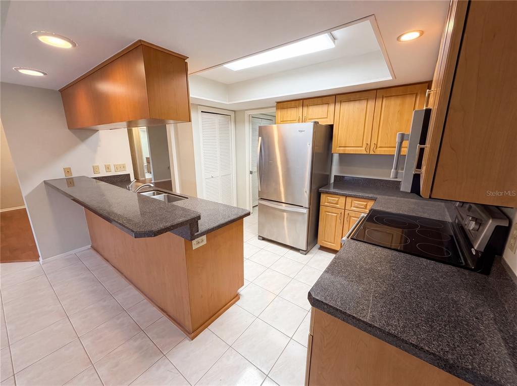 A kitchen features wood cabinets, dark countertops, stainless steel appliances, and tile flooring — 3413 SNOWY EGRET COURT, PALM HARBOR, FL