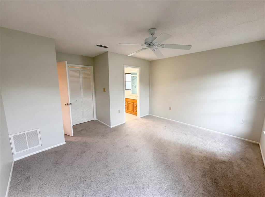An empty bedroom features gray carpet, light-colored walls, a ceiling fan, and an attached bathroom — 3413 SNOWY EGRET COURT, PALM HARBOR, FL