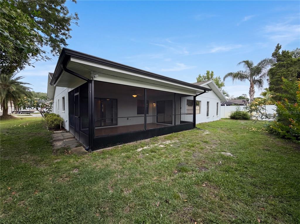 A white house features a large black-framed screened-in porch overlooking a grassy backyard — 3413 SNOWY EGRET COURT, PALM HARBOR, FL