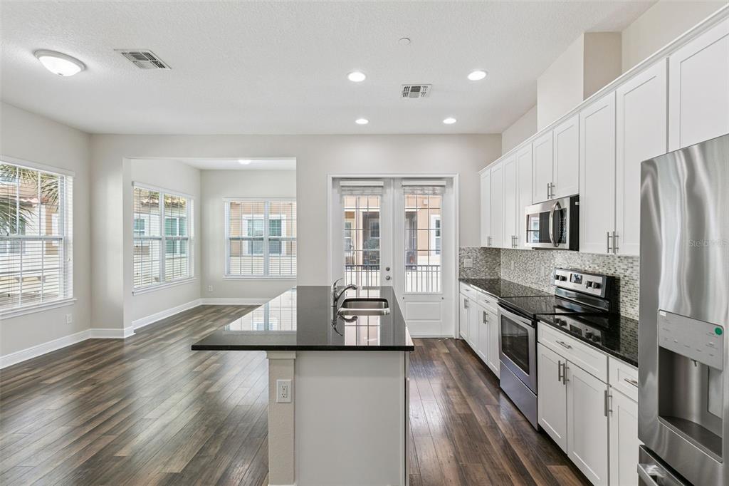 A kitchen with white cabinets, black countertops, stainless steel appliances, and dark wood-look flooring — 1016 PARMA CIRCLE, LAKE MARY, FL