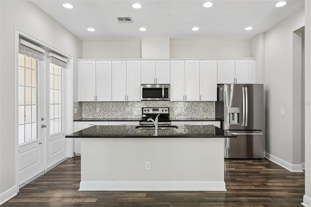 A kitchen with white cabinets, a black granite island, stainless steel appliances, and wood flooring — 1016 PARMA CIRCLE, LAKE MARY, FL