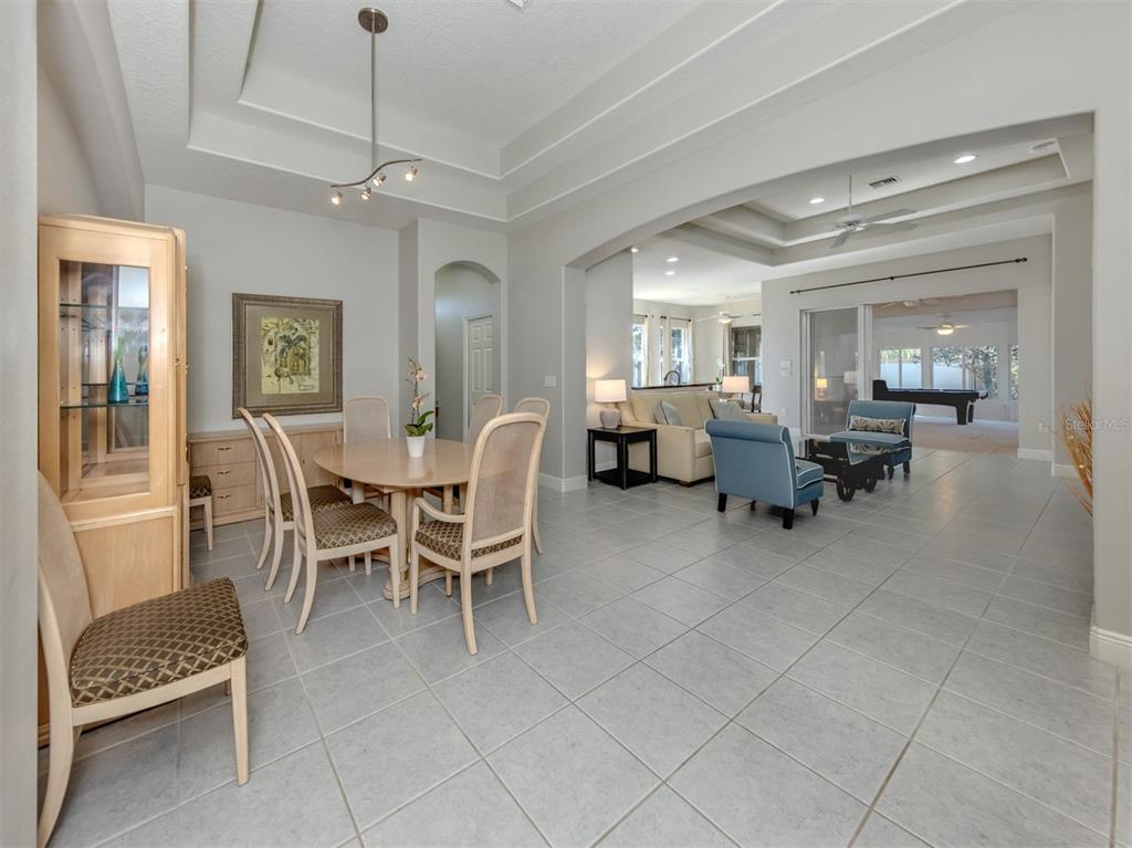 A dining area with a tray ceiling opens into a living room with tiled floors — 111 WAYFOREST DRIVE, VENICE, FL