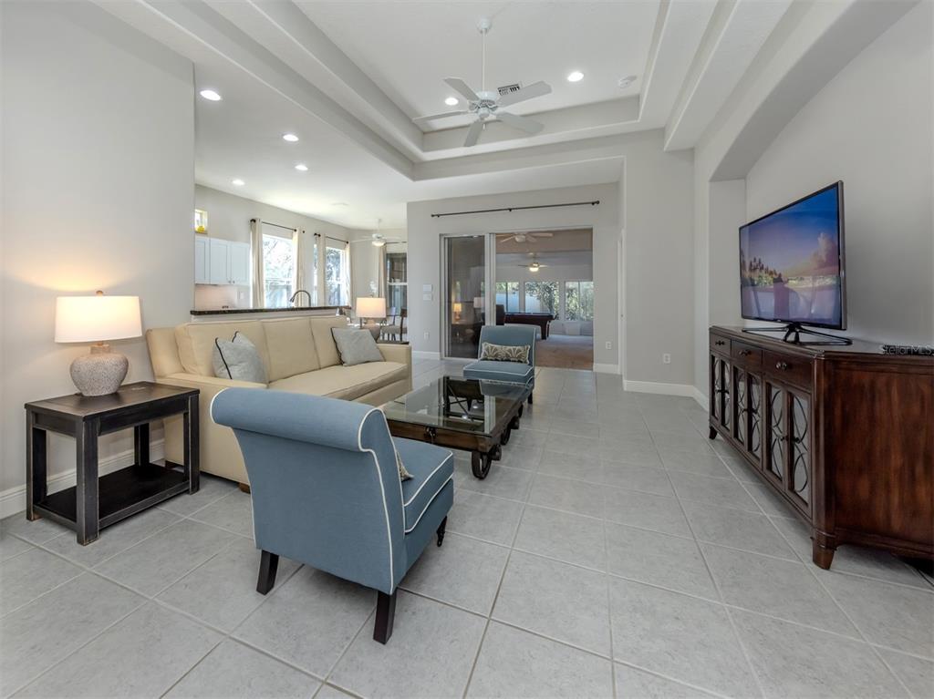 A living room features a beige sofa, blue armchairs, a glass coffee table, and tile flooring — 111 WAYFOREST DRIVE, VENICE, FL