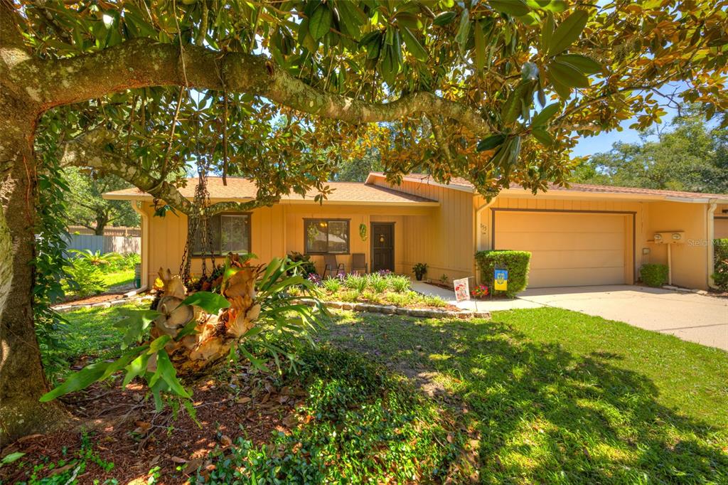 A single-story house with a tan exterior, two-car garage, and a large tree in front — 1055 W VILLAGE GREEN RD, DELAND, FL