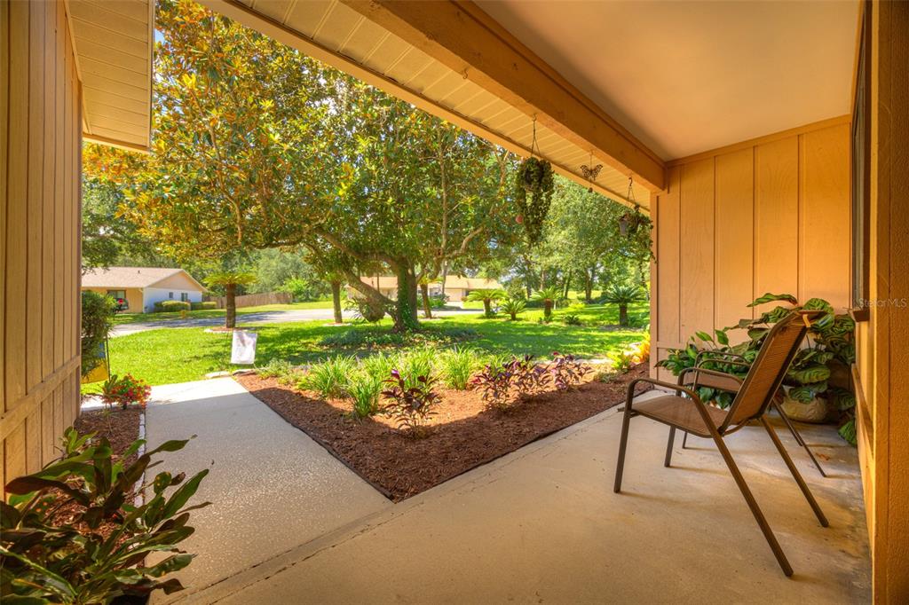 A covered concrete porch features a chair, potted plants, and a view of the yard — 1055 W VILLAGE GREEN RD, DELAND, FL