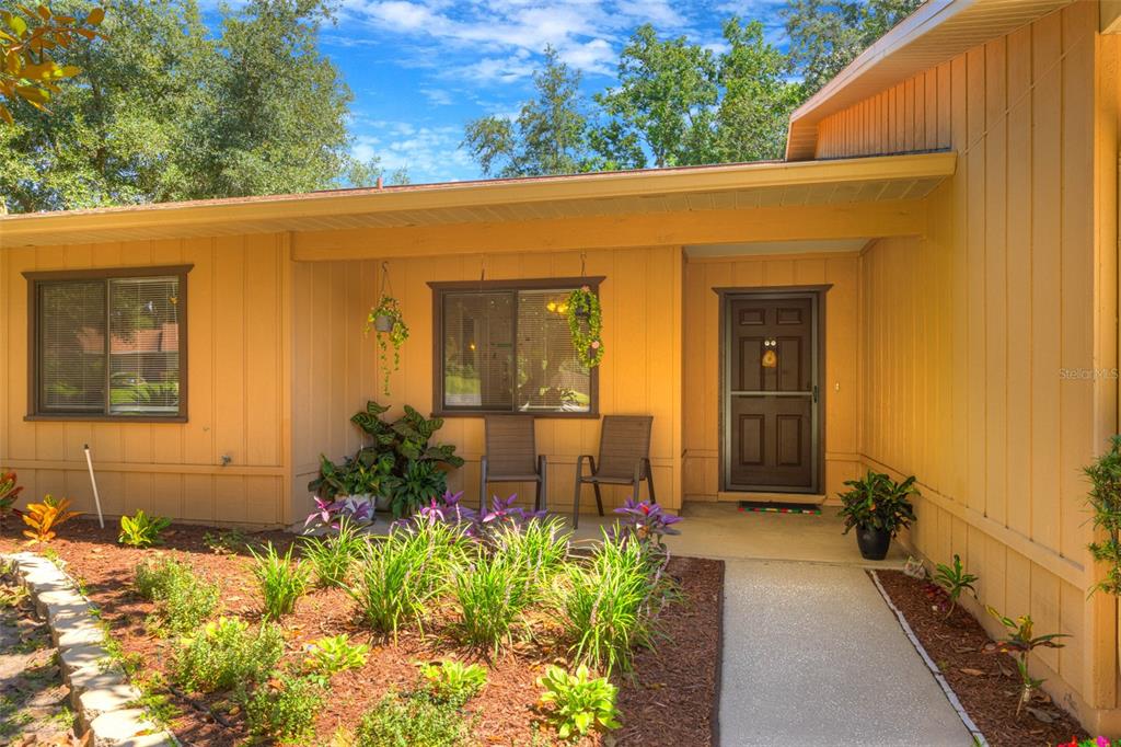 The exterior of a yellow house features a front porch, a dark door, and landscaping — 1055 W VILLAGE GREEN RD, DELAND, FL