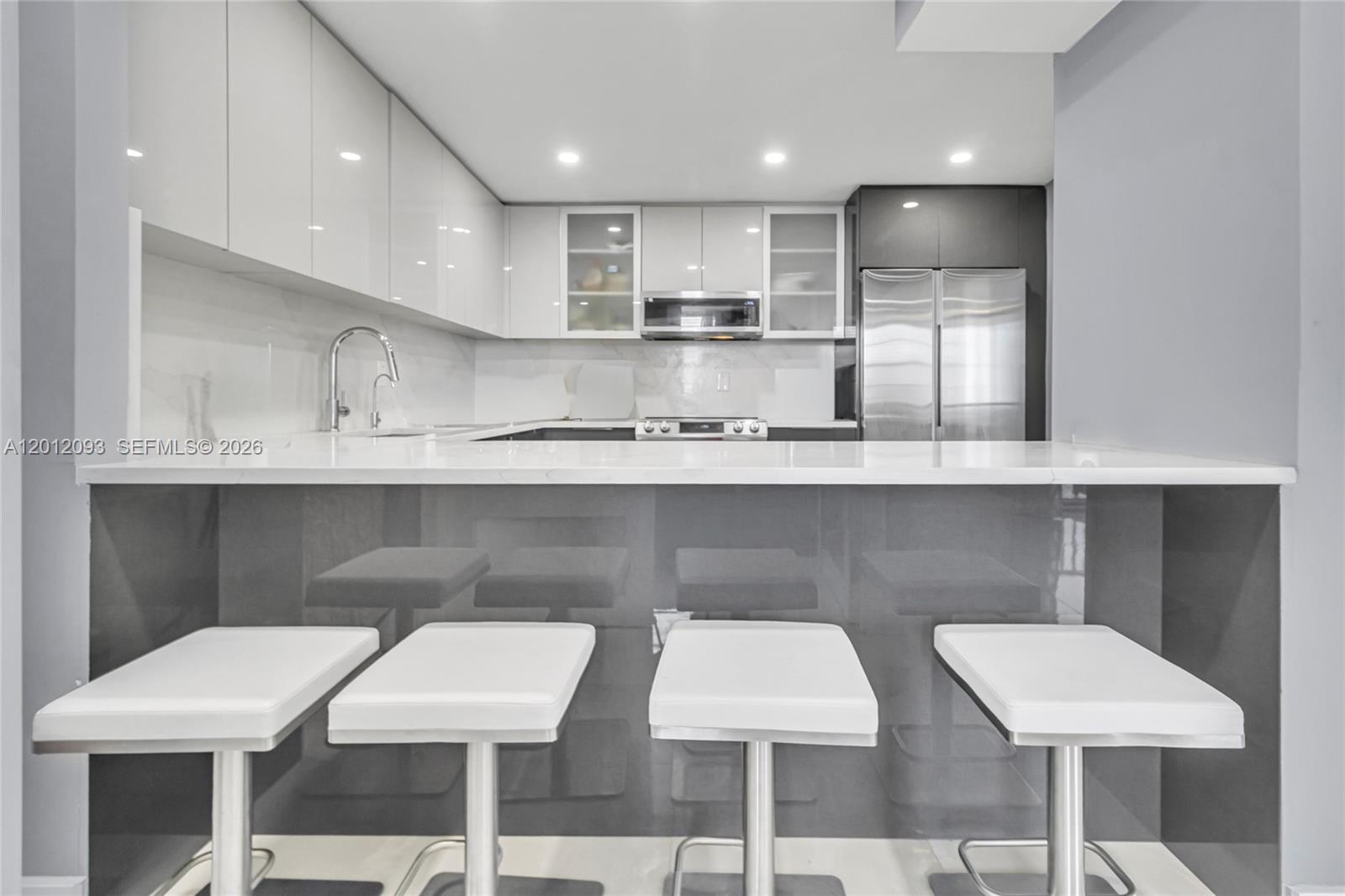 A modern kitchen features white glossy cabinets, stainless steel appliances, and a gray breakfast bar — 3161 S Ocean Dr # 1107, Hallandale Beach FL 33009, HALLANDALE BEACH, FL