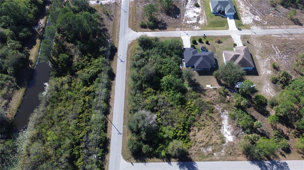 An aerial view shows a wooded residential lot next to a road and a canal — 880 GULF LANE, LEHIGH ACRES, FL