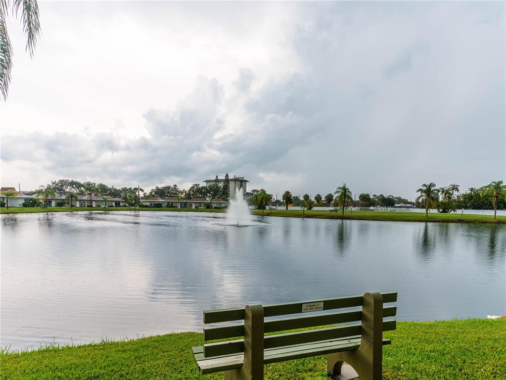 A green park bench sits on a grassy lawn overlooking a pond with a fountain — 4318 TAHITIAN GARDENS CIRCLE UNIT F, HOLIDAY, FL