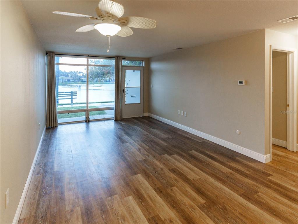 An empty living room features wood-look flooring, a ceiling fan, and a sliding glass door — 4318 TAHITIAN GARDENS CIRCLE UNIT F, HOLIDAY, FL