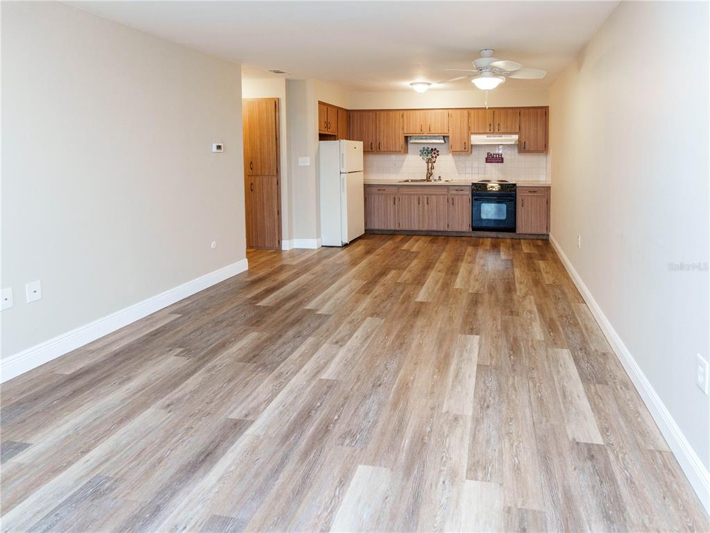 A kitchen with wood-look flooring, light-colored walls, and wooden cabinets opens into a living area — 4318 TAHITIAN GARDENS CIRCLE UNIT F, HOLIDAY, FL