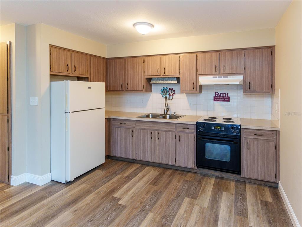 A kitchen features wood-grain cabinets, a white refrigerator, a black stove, and light-colored flooring — 4318 TAHITIAN GARDENS CIRCLE UNIT F, HOLIDAY, FL