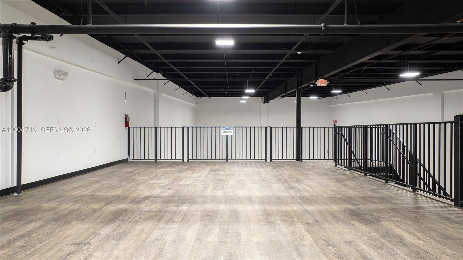 An open mezzanine level features wood-look flooring, black metal railings, and an exposed ceiling — 7265 NW 74th St # 6, Medley FL 33166, MEDLEY, FL