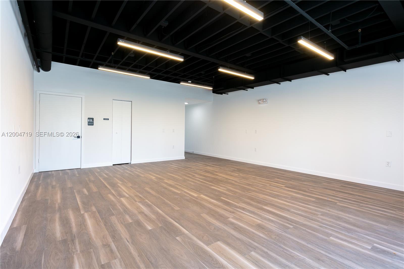 An empty room features white walls, wood-look flooring, and a black exposed ceiling with lights — 7265 NW 74th St # 6, Medley FL 33166, MEDLEY, FL