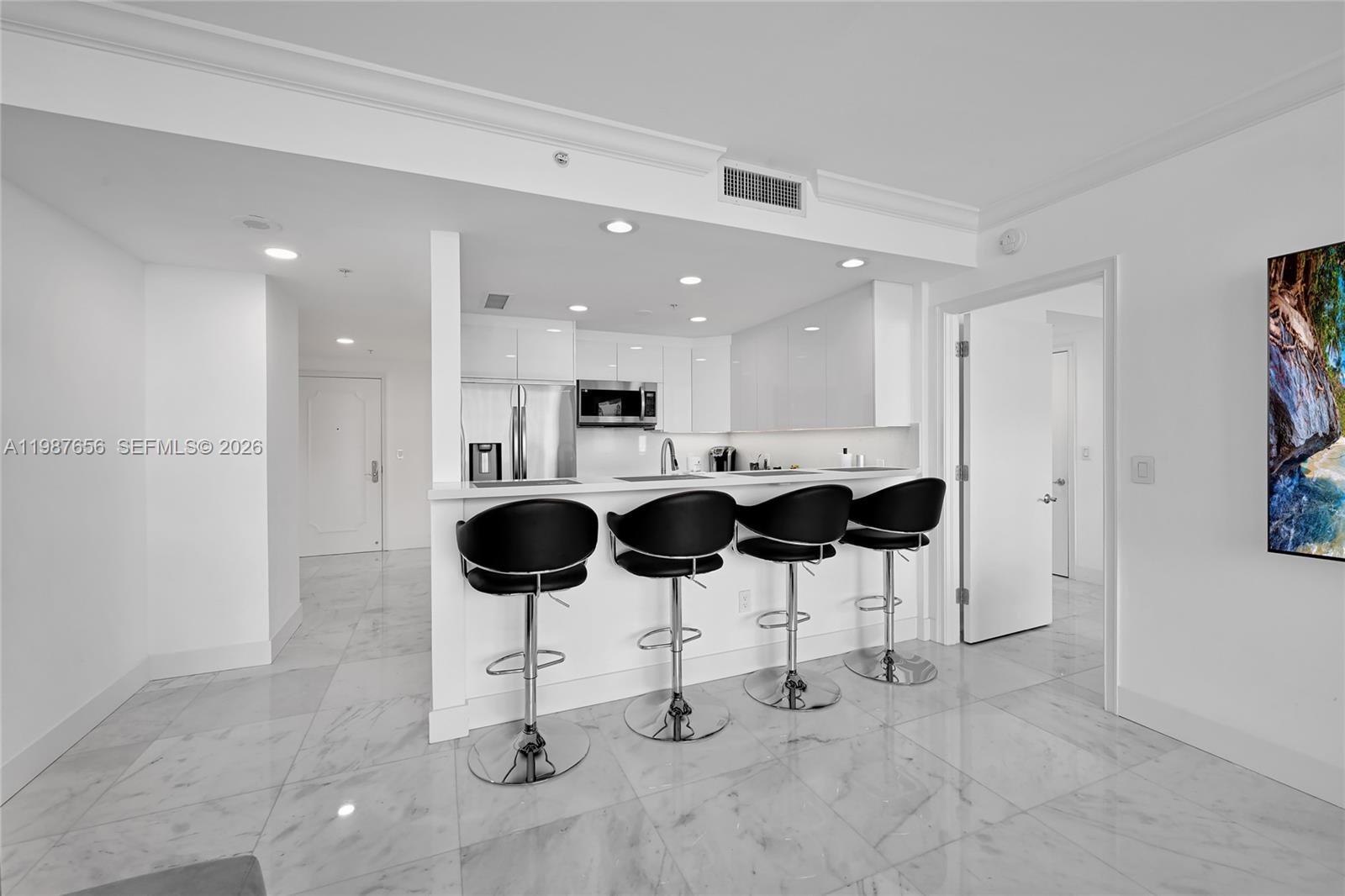 A modern kitchen features white cabinetry, a breakfast bar with four stools, and marble flooring — 3350 SW 27th Ave # 1908, Coconut Grove FL 33133, COCONUT GROVE, FL