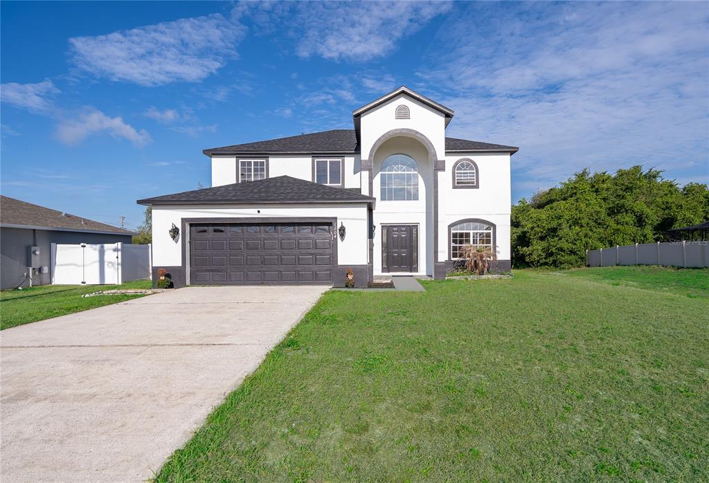 A two-story house with white stucco walls, a dark garage door, and a concrete driveway — 1204 APOPKA DRIVE, POINCIANA, FL