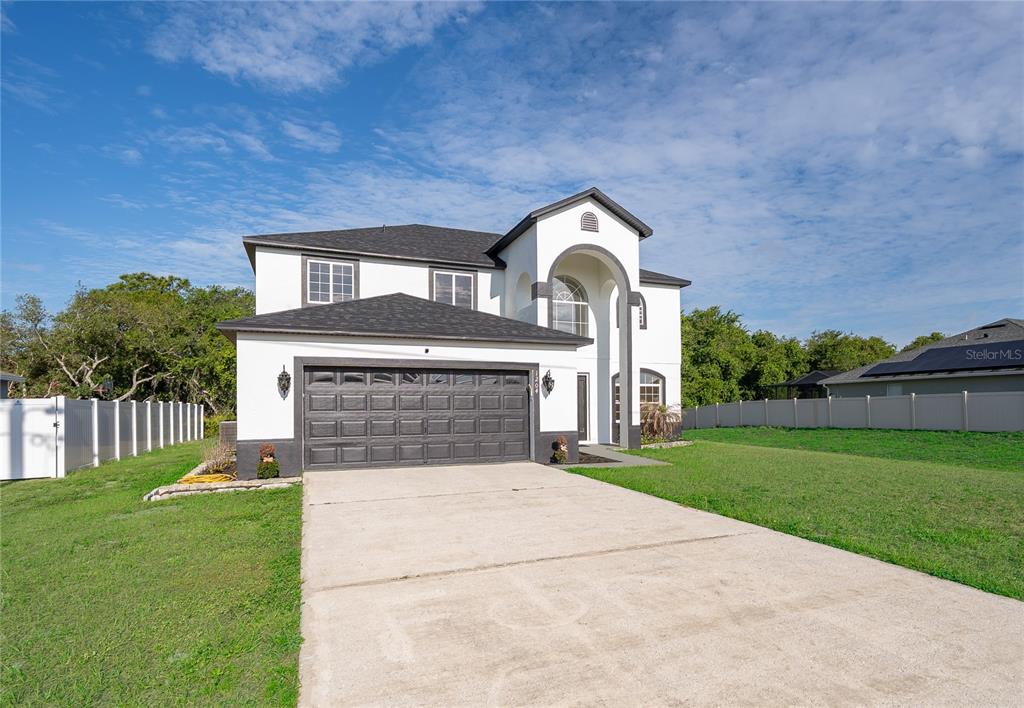 A two-story house with a dark garage door, white stucco exterior, and a concrete driveway — 1204 APOPKA DRIVE, POINCIANA, FL