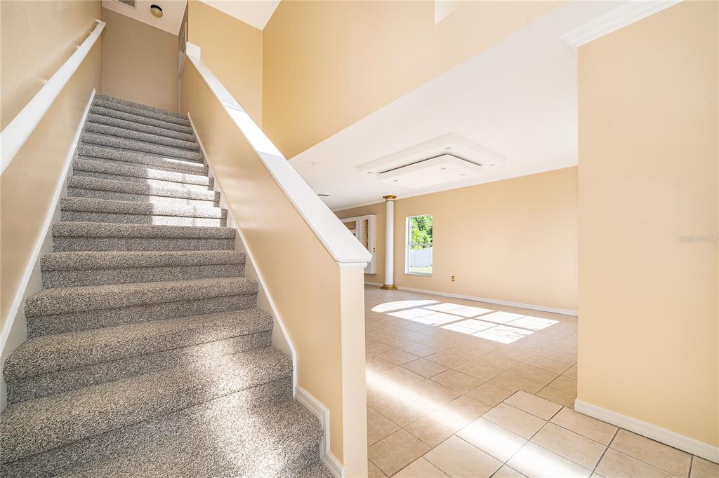 A carpeted staircase leads to an upper level next to an open, tiled living area — 1204 APOPKA DRIVE, POINCIANA, FL