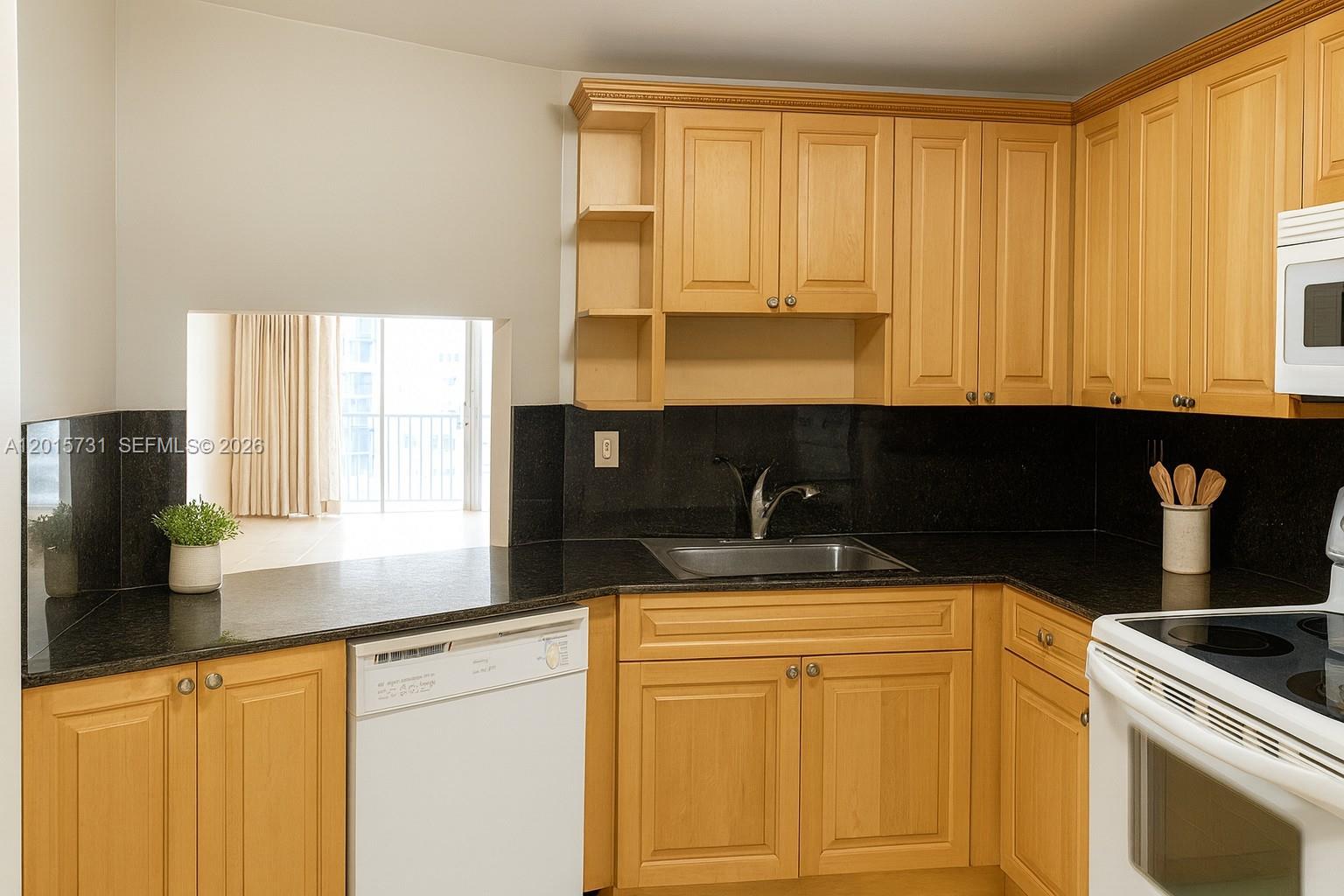 A kitchen features light wood cabinets, black countertops, a white dishwasher, and a pass-through window — 1750 NE 191st St # 3, Miami FL 33179, MIAMI, FL
