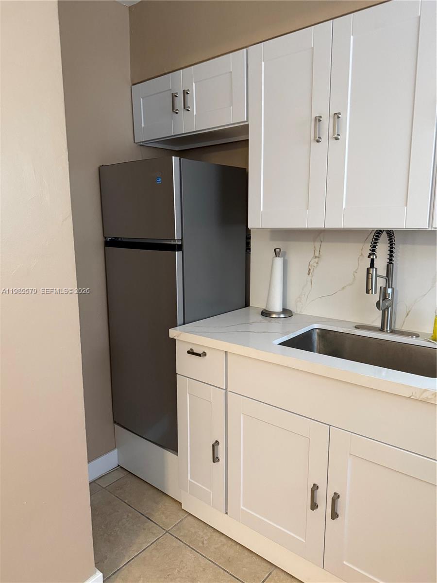 A small kitchen features white cabinets, a stainless steel refrigerator, and a marble-look countertop — 321 Wilson St # A204, Hollywood FL 33019, HOLLYWOOD, FL