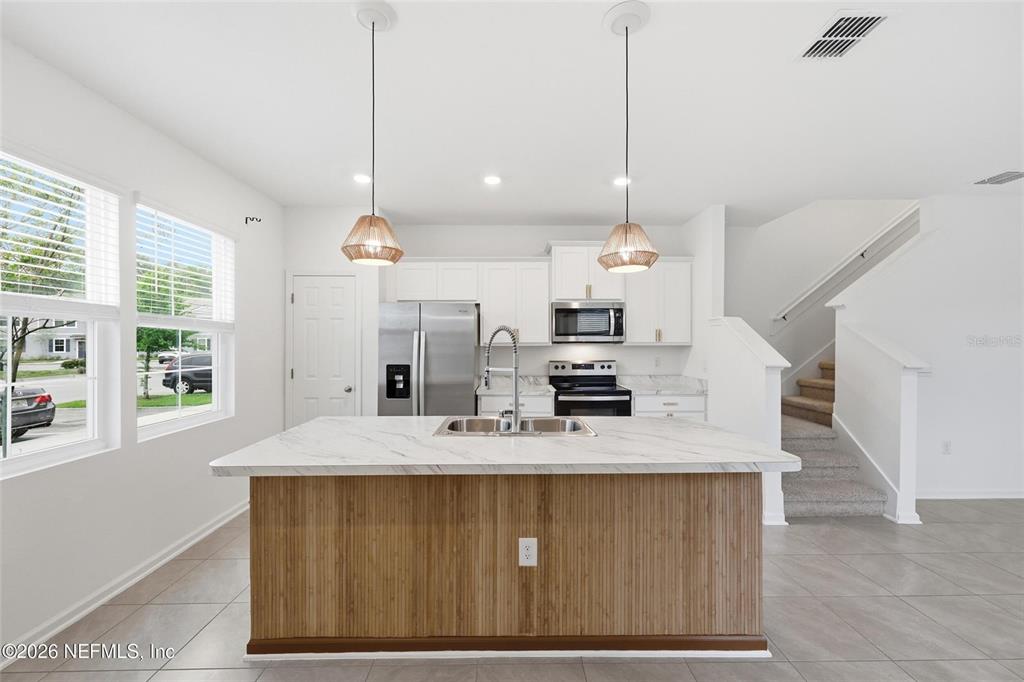 A kitchen features a wood-paneled island, white cabinetry, stainless steel appliances, and tile flooring — 4935 NEBULA LANE, JACKSONVILLE, FL