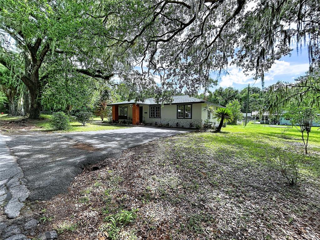 A single-story house with a brick entrance and stone facade sits under large oak trees — 524 EAST AVENUE, BROOKSVILLE, FL
