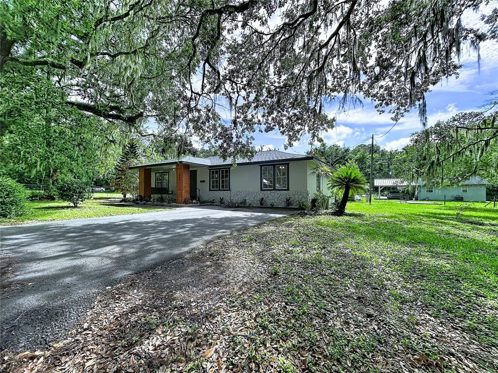 A single-story house with a gravel driveway sits under large oak trees — 524 EAST AVENUE, BROOKSVILLE, FL