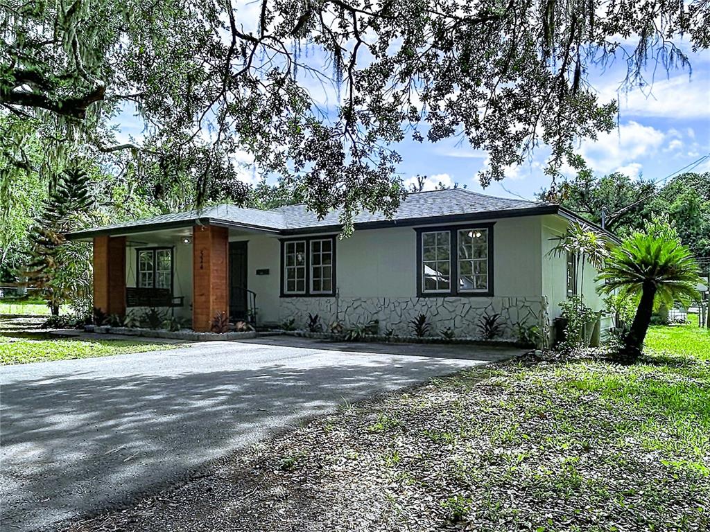 A single-story house with a stone facade, dark trim, and a covered porch under trees — 524 EAST AVENUE, BROOKSVILLE, FL