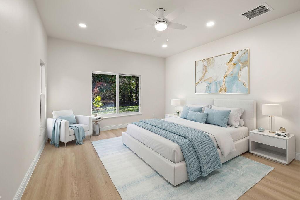 A modern bedroom features a white bed, light wood floors, and a large window — 4805 66th Lane, Vero Beach FL 32967, VERO BEACH, FL