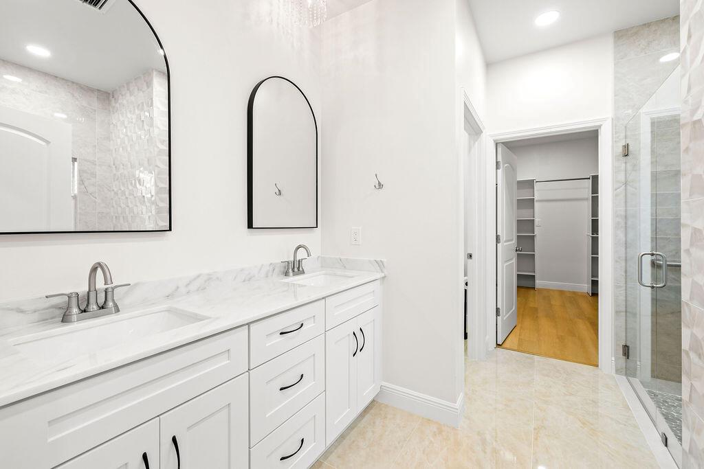 A modern bathroom features a white double vanity with marble countertops and arched wall mirrors — 4805 66th Lane, Vero Beach FL 32967, VERO BEACH, FL