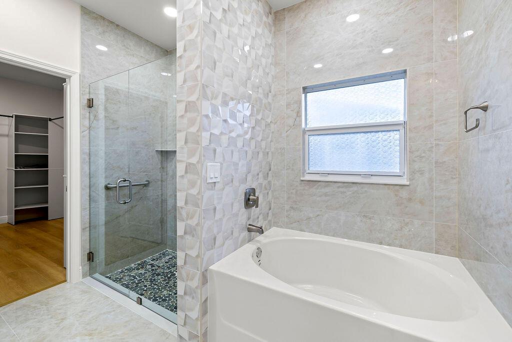 A bathroom features a glass-enclosed shower with pebble flooring next to a white soaking tub — 4805 66th Lane, Vero Beach FL 32967, VERO BEACH, FL