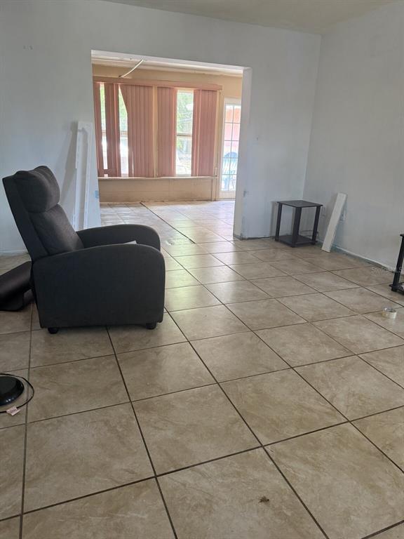 A living room with light tile flooring leads into a sunroom with vertical blinds — 2509 25TH AVENUE W, BRADENTON, FL