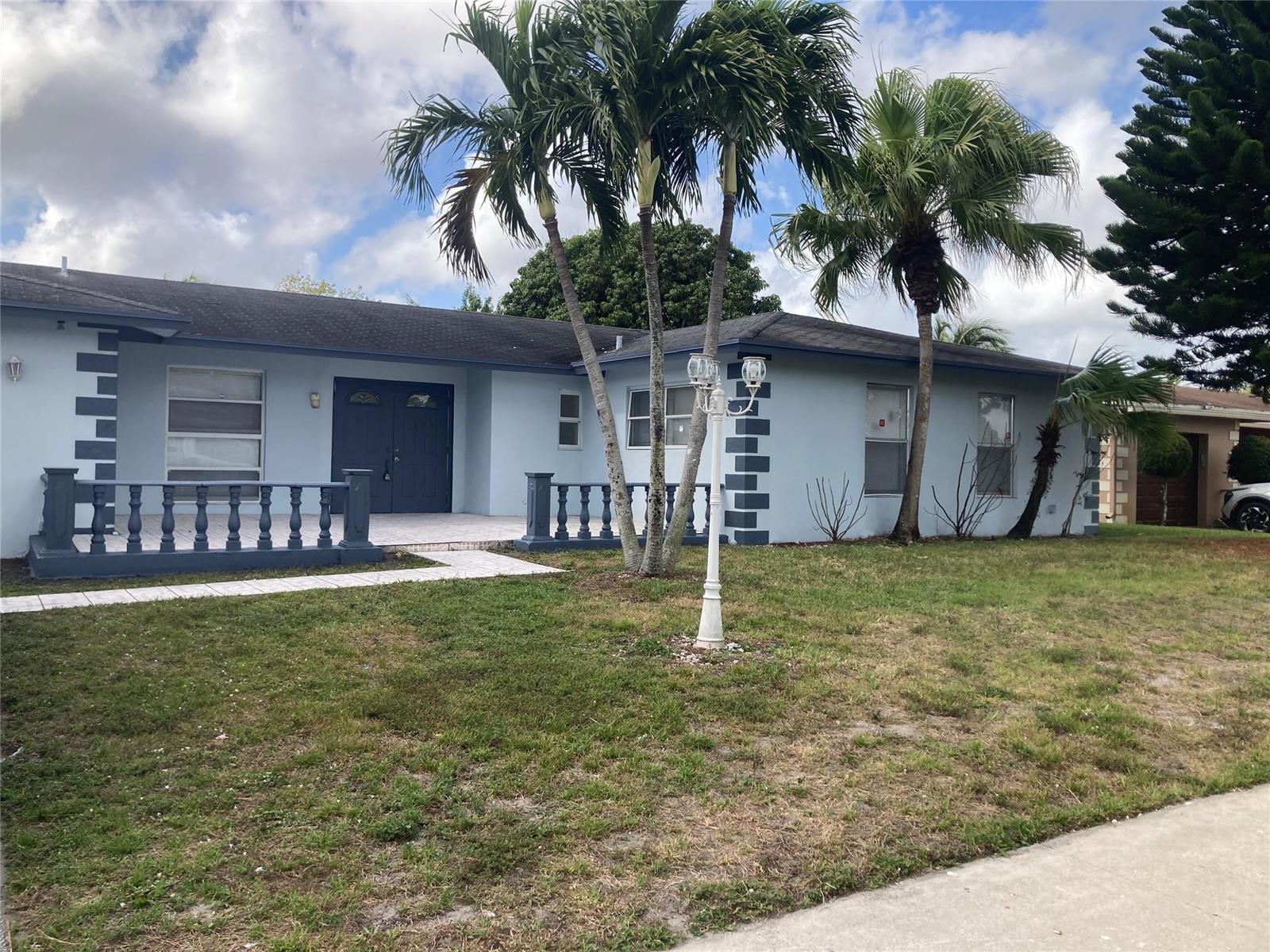 A light blue single-story house features a front porch with dark blue balustrades and palms — 6230 SW 4th Place, Margate FL 33068, MARGATE, FL