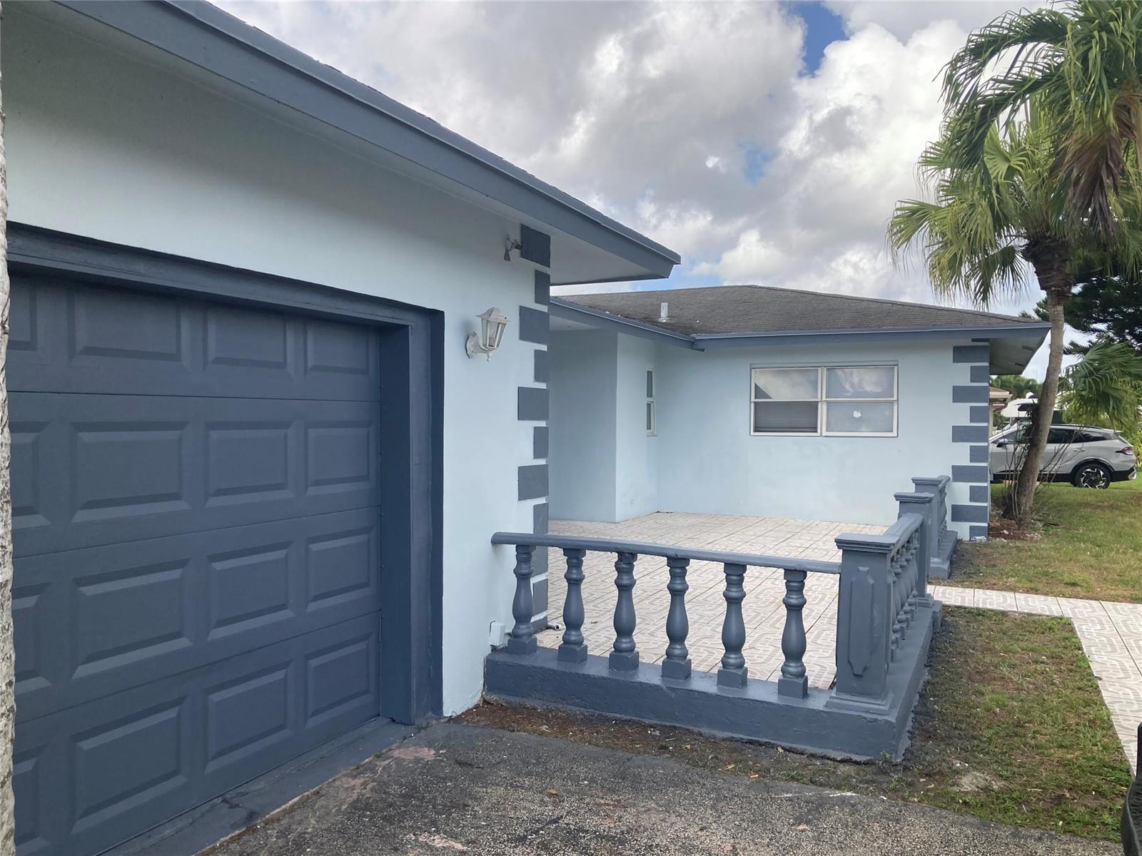 A light blue house exterior features a dark gray garage door and a front patio — 6230 SW 4th Place, Margate FL 33068, MARGATE, FL