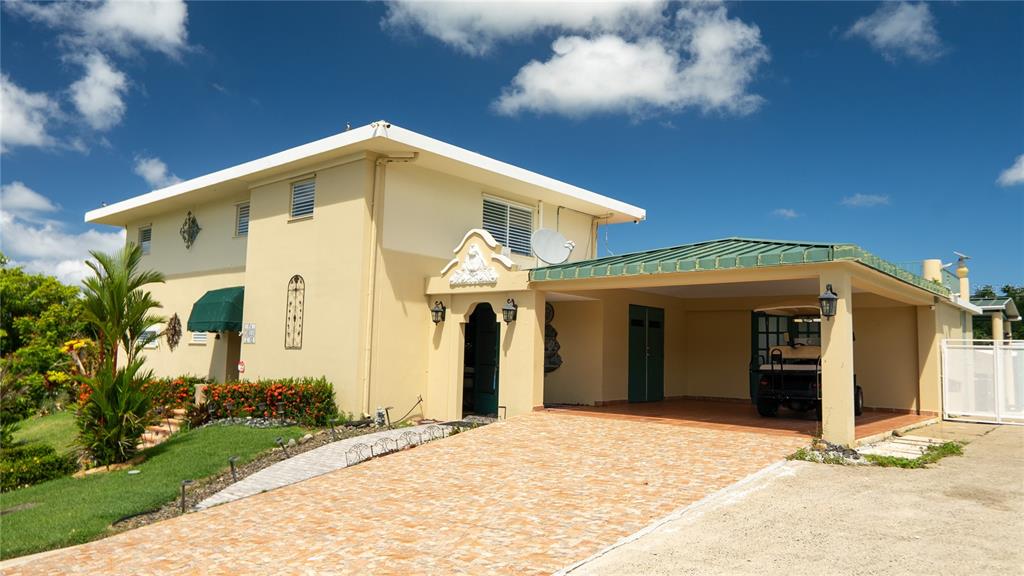 A two-story yellow house features a covered carport, a tiled driveway, and a green awning — #12 CALLE CENTRAL HACIENDA MARGARITA, LUQUILLO, PR