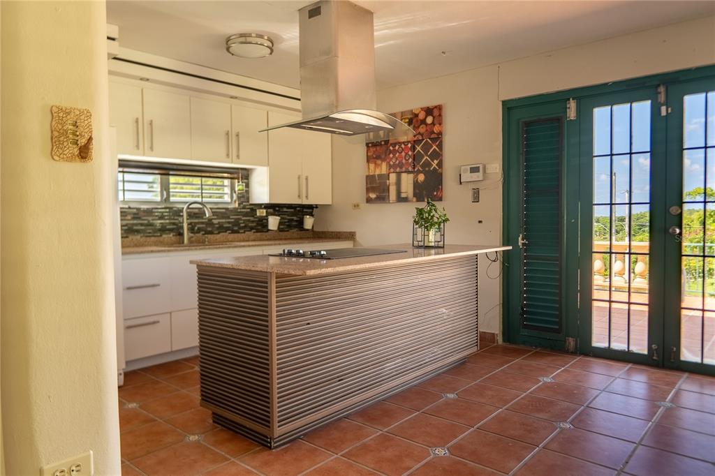 A kitchen features a central island with a cooktop, white cabinetry, and terracotta tile flooring — #12 CALLE CENTRAL HACIENDA MARGARITA, LUQUILLO, PR