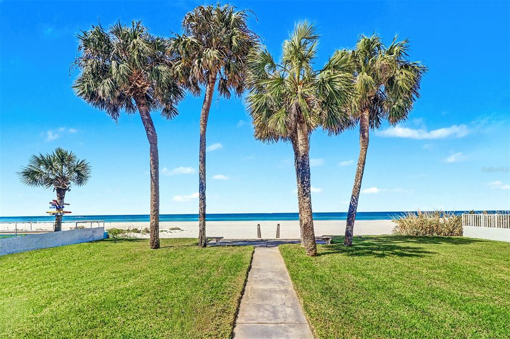 A concrete path leads through a grassy lawn toward palm trees and a sandy beach — 18206 SUNSET BOULEVARD, REDINGTON SHORES, FL