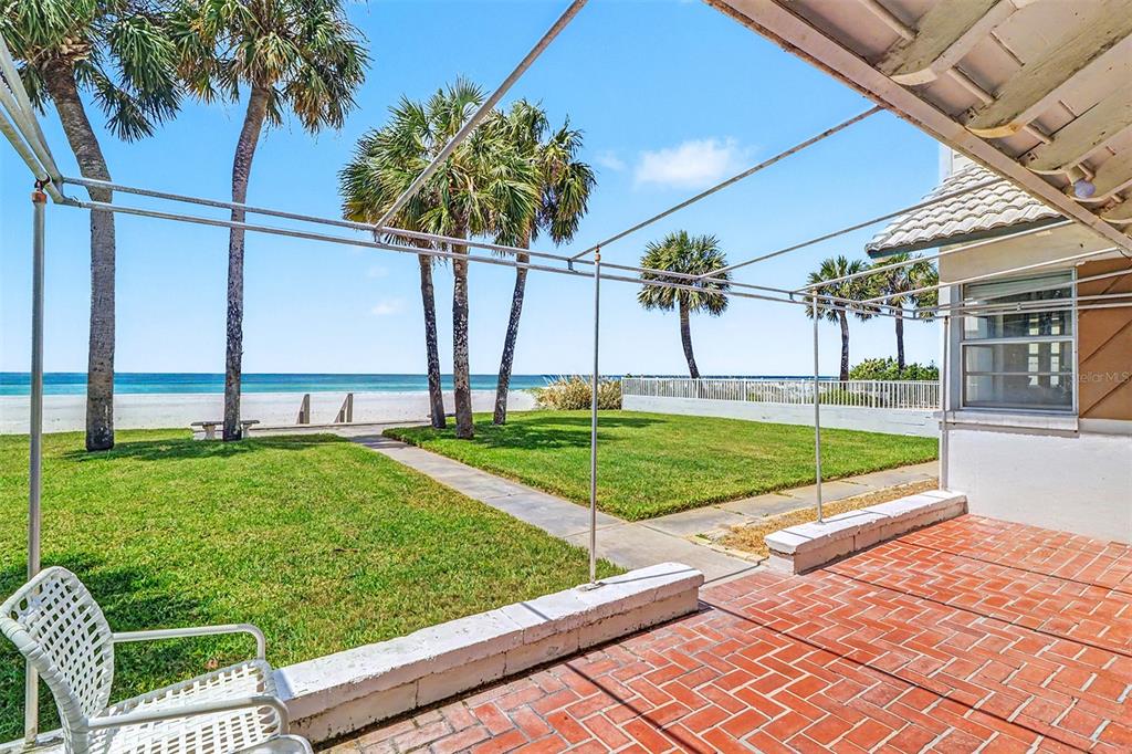 A brick patio overlooks a grassy lawn, palm trees, and the ocean beyond — 18206 SUNSET BOULEVARD, REDINGTON SHORES, FL