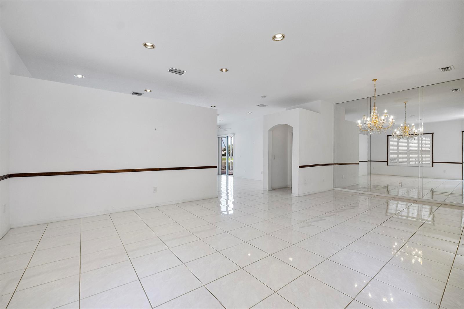 An empty room with white tile floors, a mirrored wall, and a crystal chandelier — 7591 NW 59th Way, Parkland FL 33067, PARKLAND, FL
