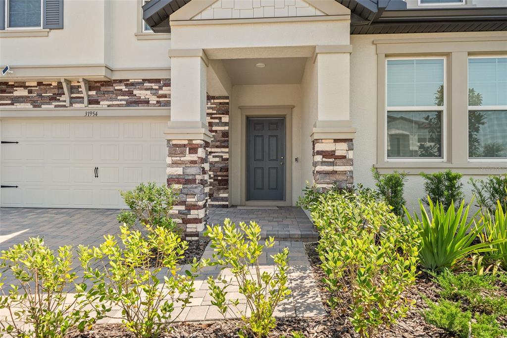 The exterior of a house features a stone-accented entryway, a gray front door, and landscaping — 31954 SAPNA CHIME DRIVE, WESLEY CHAPEL, FL