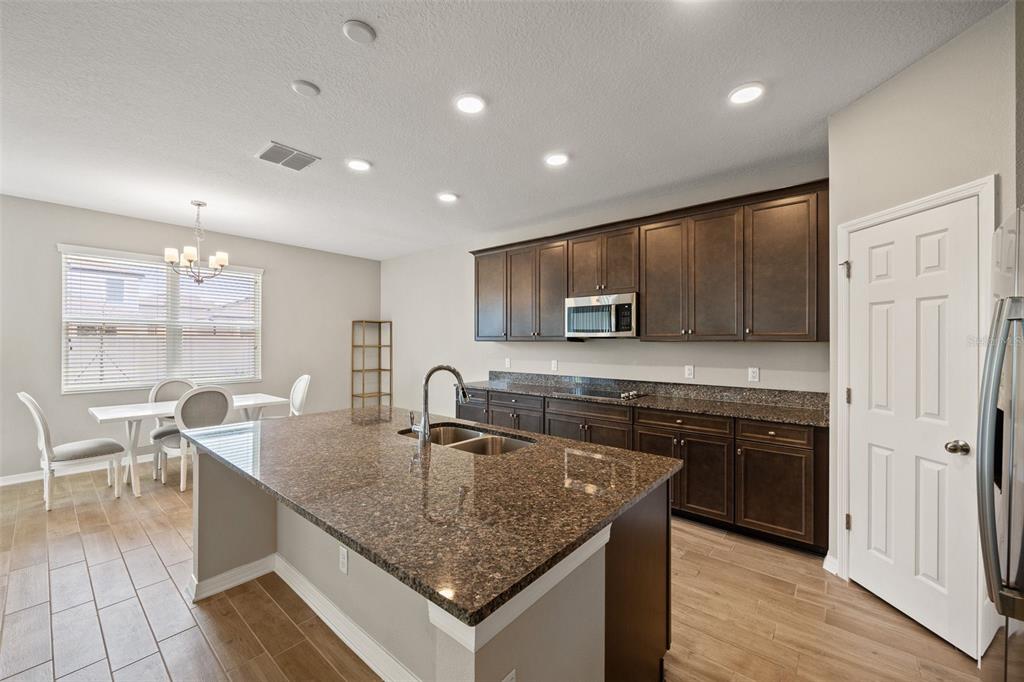 A kitchen features dark wood cabinets, granite countertops, a center island, and light tile flooring — 31954 SAPNA CHIME DRIVE, WESLEY CHAPEL, FL