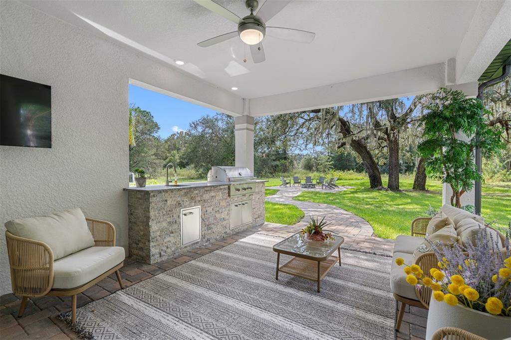 A covered patio features a stone outdoor kitchen, seating area, and a view of the yard — 13055 OLDENBURG DRIVE, HUDSON, FL