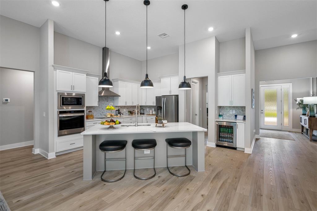 A modern kitchen features white cabinets, a central island with bar seating, and stainless appliances — 13055 OLDENBURG DRIVE, HUDSON, FL