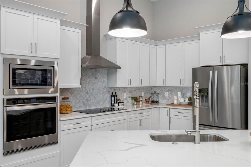 A modern kitchen features white cabinetry, stainless steel appliances, a marble backsplash, and a quartz island — 13055 OLDENBURG DRIVE, HUDSON, FL