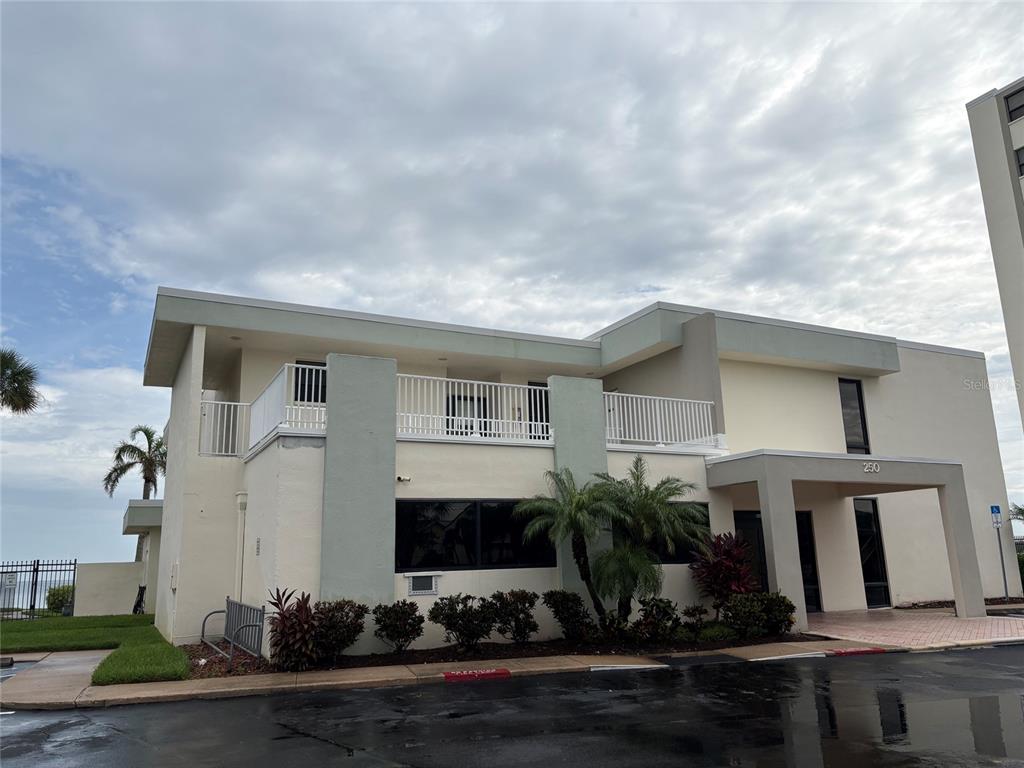 A two-story building with a white balcony and a covered entrance under a cloudy sky — 250 WOODETTE DRIVE UNIT A, DUNEDIN, FL