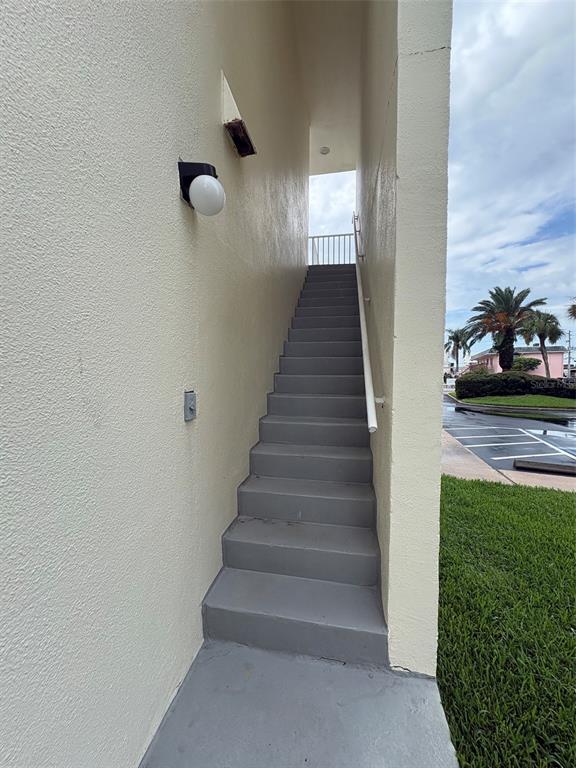 An exterior staircase with grey steps leads upward between two beige stucco walls — 250 WOODETTE DRIVE UNIT A, DUNEDIN, FL