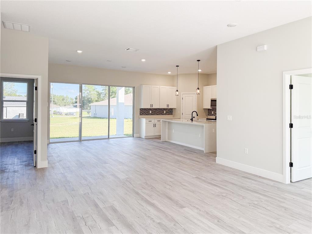 An open-concept living area features light wood-look flooring, white cabinetry, and a sliding glass door — 6243 SW 133RD STREET ROAD, OCALA, FL