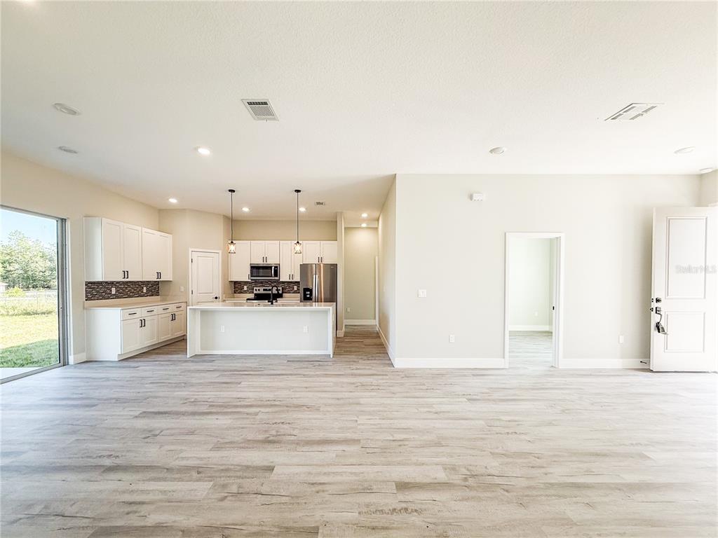 An open-concept kitchen with white cabinetry, a central island, and light wood-look flooring — 6243 SW 133RD STREET ROAD, OCALA, FL