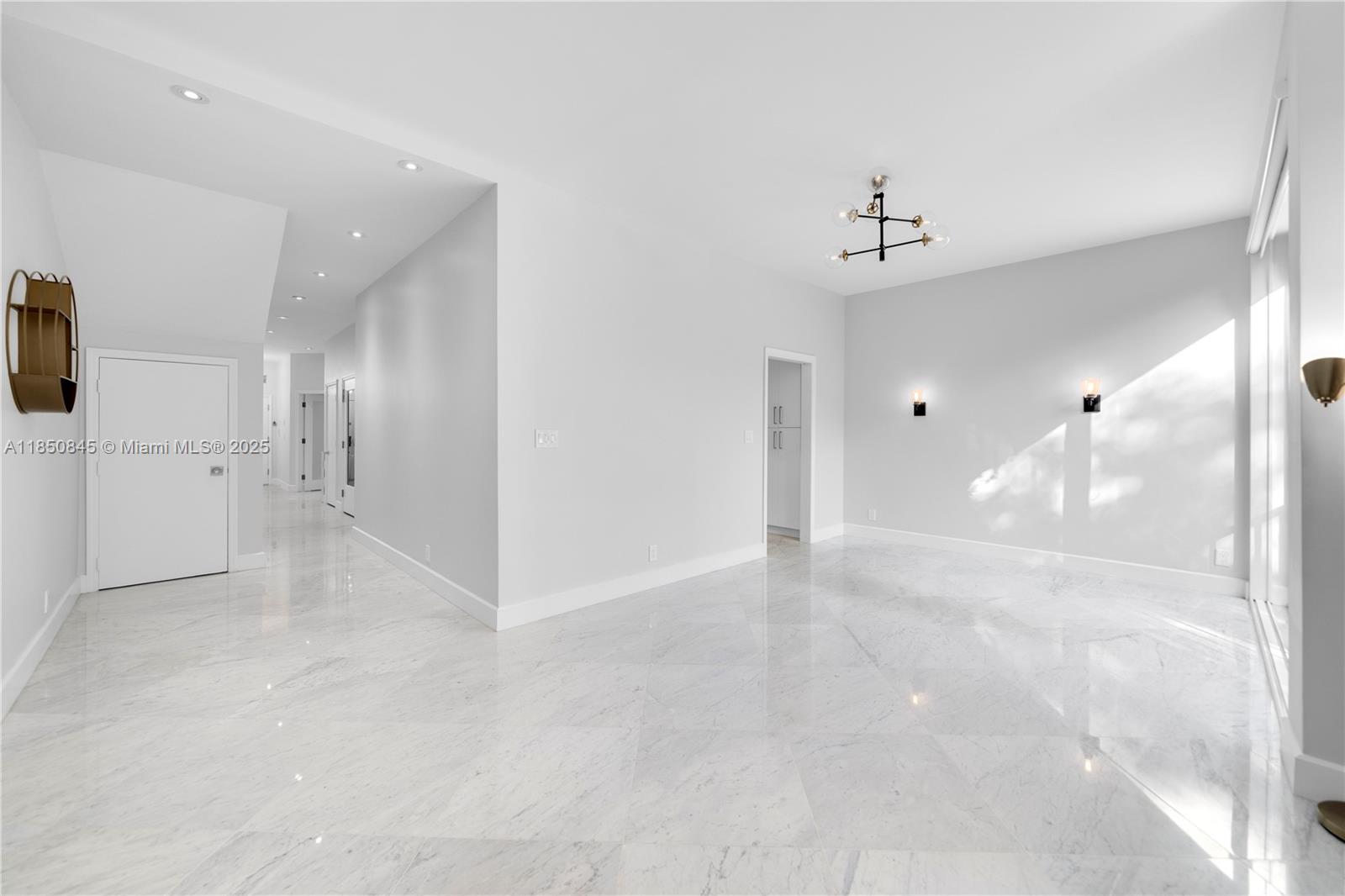 A bright, minimalist room features white marble flooring, recessed lighting, and a modern chandelier — 1558 NE Quayside Ter # D10, Miami FL 33138, MIAMI, FL
