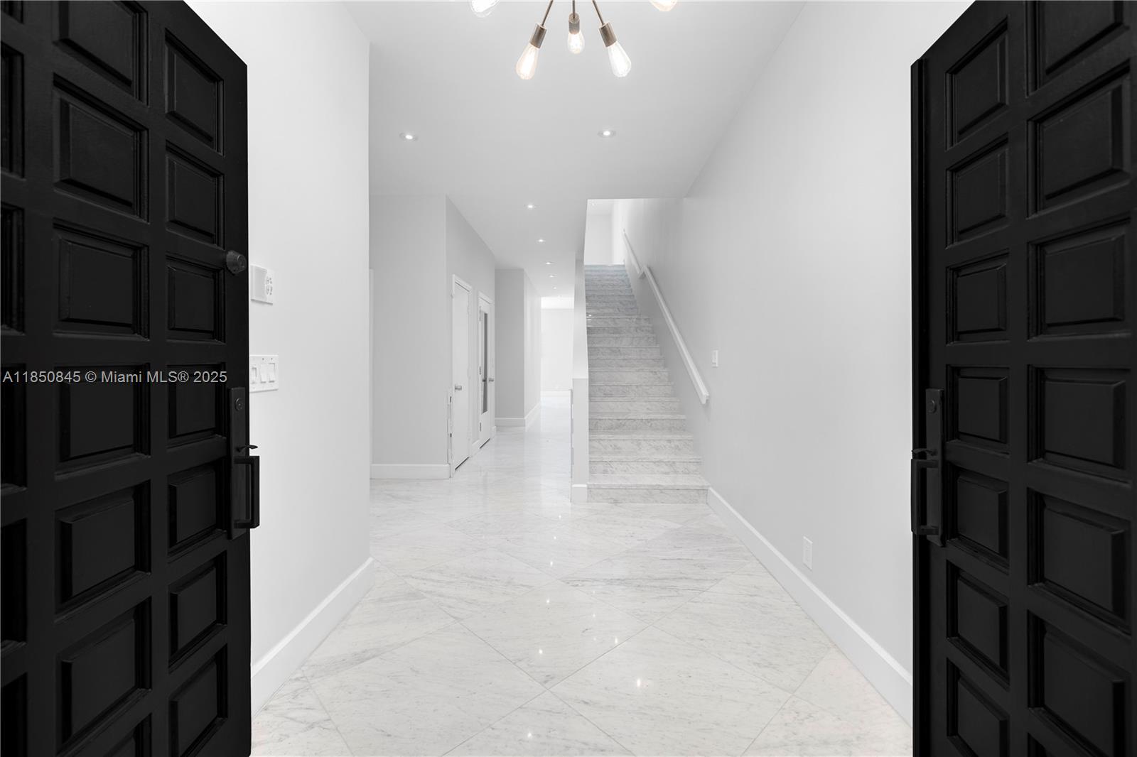A modern entryway features white marble flooring, black paneled doors, and a staircase — 1558 NE Quayside Ter # D10, Miami FL 33138, MIAMI, FL